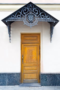View on a porch with brown wooden door and forged decorative lattice on the pediment photo