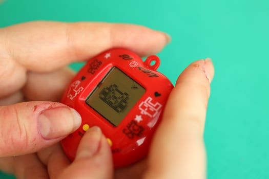 KYIV, UKRAINE - MARCH 9, 2024 Retro pet keychain game tamagotchi in red plastic case in female hands photo