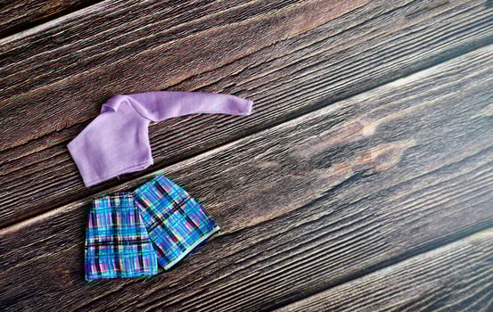 One shoulder purple crop top shirt and striped blue short pants. Small human doll fashion clothing object isolated on dark wooden surface table background. photo