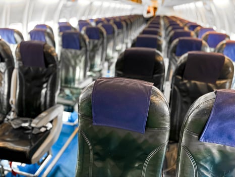 Interior view of empty airplane cabin with rows of black leather seats and blue headrest covers, illuminated by overhead lights, showing aisle running down middle and windows on both sides. photo