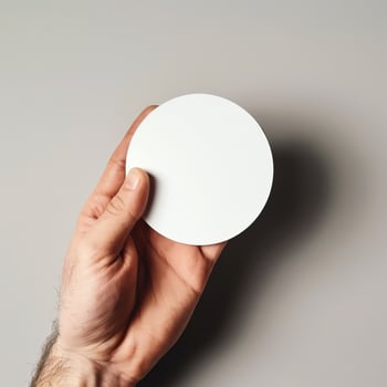 Close-up of a hand holding a blank white circular card against a neutral background. Ideal for mockups, designs, and message presentations. photo