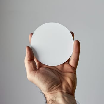 Hand holding a blank white circle card against a neutral background for copy space and design mockup. photo