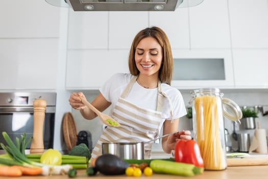 Joyful Young Lady Cooking and Sampling Dinner in a Pot, Present in a Contemporary Home Kitchen. Homemaker Preparing Nutritious Meal with a Smile. Domestic Life and Nourishment. Healthy Eating. photo