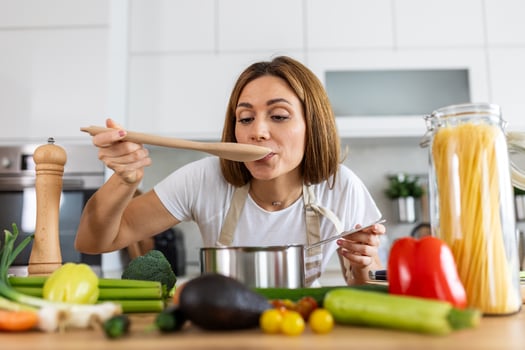 Joyful Young Lady Cooking and Sampling Dinner in a Pot, Present in a Contemporary Home Kitchen. Homemaker Preparing Nutritious Meal with a Smile. Domestic Life and Nourishment. Healthy Eating. photo