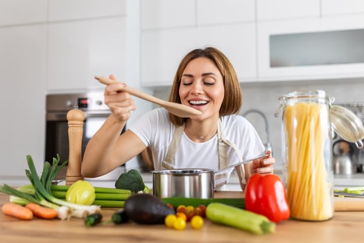 Happy Young Woman Cooking Tasting Dinner In A Pot Standing In Modern Kitchen At Home. Housewife Preparing Healthy Food Smiling . Household And Nutrition. Dieting Recipes Concept photo