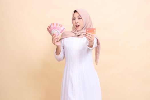 Muslim woman indonesia in hijab looks elegant holding rupiah cash and credit card in hand. Lifestyle, religious, business and finance concepts photo