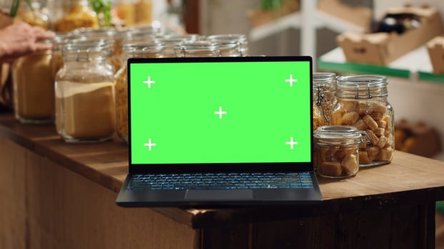 Chroma key laptop with copy space used as commercial sign in low carbon footprint local shop. Promotional ad on green screen device in food store with products in recyclable glass containers photo