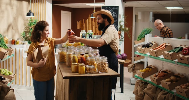 Client talking with seller in organic food shop, inquiring about products ethical sourcing and asking for recommendations. Woman in low carbon footprint store chatting with trader about pantry staples photo
