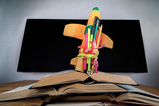 cardboard rocket and pencils over books in front of classroom blackboard photo