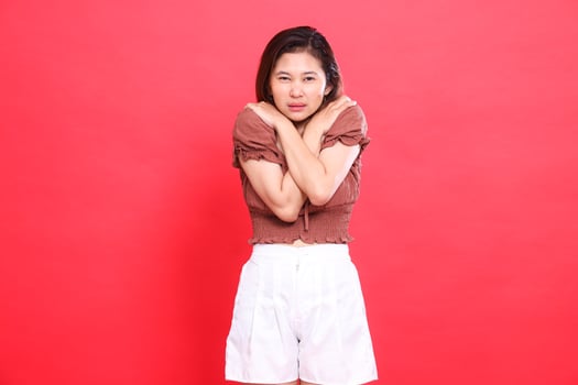 Asian woman's expression, candid, fear, body, shivering, fever, catching a cold, wearing a brown blouse and shorts on a red background. for health, lifestyle and advertising concepts photo