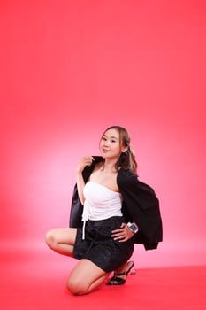 full portrait of young Asian girl in office, career, squatting, smiling, covered in black jacket, hands to jacket and waist, for corporate, fashion, commercial, agency content photo
