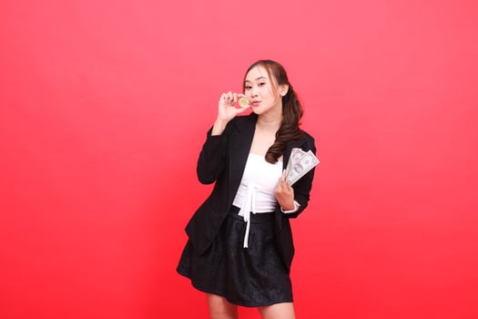 young Asian office female gestures to the camera wearing a black formal suit, hands holding dollar bills and kissing bitcoin, for financial content, business, advertising, investment photo