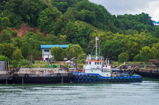 Batam, Indonesia. July 12, 2024. Tugboats and barges are docked, with a mountain background with lush trees photo
