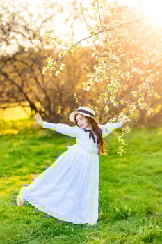 A happy girl in a white dress and a hat dancing under flowering trees in the garden photo