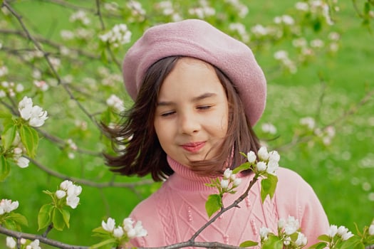 A happy little girl stands with her eyes closed in a blooming white apple tree in the park. photo