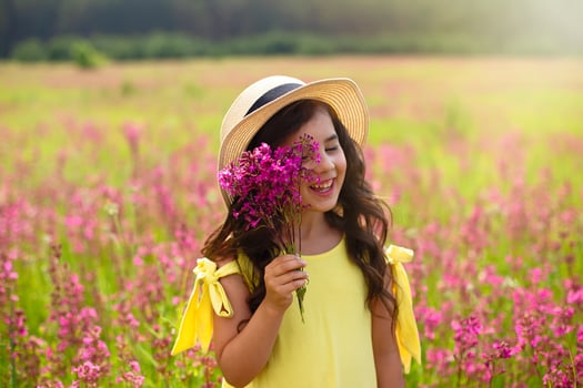 A beautiful playful little girl in a straw hat, holds a bouquet of burgundy viscaria flowers photo