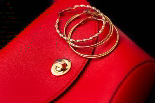 Gold ring earrings lie on a red leather bag photo
