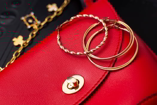 Gold ring earrings and costume jewelry lie on a red leather bag photo
