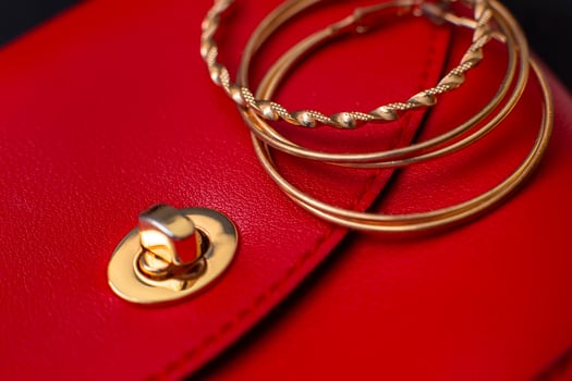Three gold hoop earrings lie on a red leather bag photo