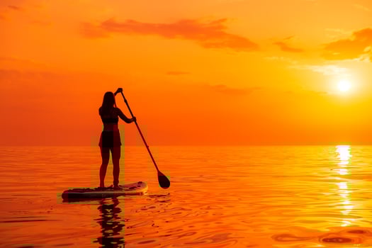 June 25, 2021. Anapa, Russia. Woman walking on paddle board at quiet sea with sunset or sunrise. Woman on Red Paddle sup board and sunset with reflection photo