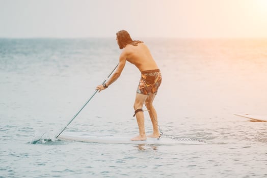 Sea woman and man on sup. Silhouette of happy young woman and man, surfing on SUP board, confident paddling through water surface. Idyllic sunset. Active lifestyle at sea or river. photo