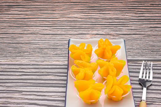Pinched Gold Egg Yolks or Khanom Thong Yip in the Thai language are placed on a plate with cutlery placed on wooden table background. Thai dessert photo
