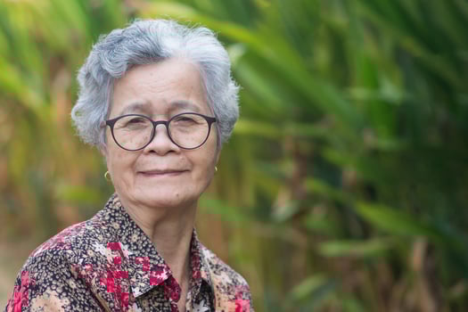 Portrait of a beautiful senior woman with short gray hair, wearing glasses, smiling, and looking at the camera while standing in a garden. Space for text. Concept of aged people and relaxation photo
