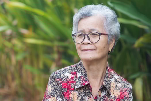 Portrait of a beautiful senior woman with short gray hair, wearing glasses, smiling, and looking at the camera while standing in a garden. Space for text. Concept of aged people and relaxation photo