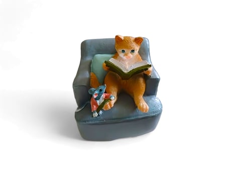 Decorative miniature cat reading on a sofa with a mouse on a white background photo