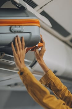 Young Female Tourist Storing Luggage in Overhead Compartment on Airplane During Travel photo