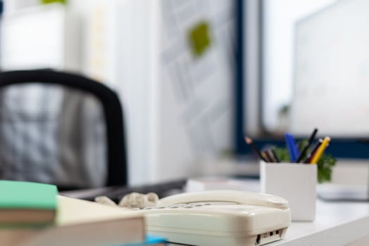 Closeup of phone on desk in empty business office. Startup workspace furniture in indoors work location. Modern commercial workplace design with telephone on white table with supplies. photo