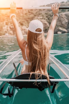 Woman in kayak back view. Happy young woman with long hair floating in transparent kayak on the crystal clear sea. Summer holiday vacation and cheerful female people relaxing having fun on the boat photo