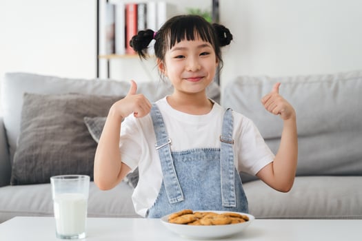 A young girl is sitting at a table with a glass of milk and a plate of cookies photo