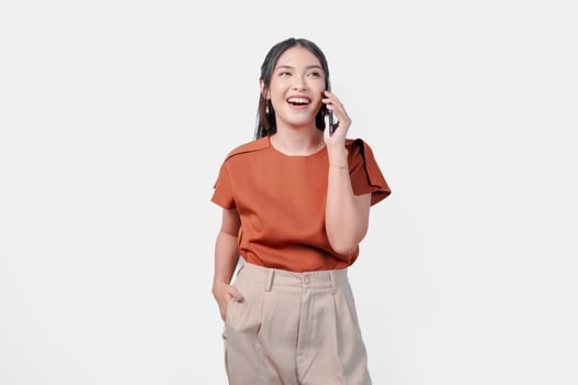 Cheerful young Asian woman wearing brown shirt smiling and having a call with someone, isolated by white background. photo
