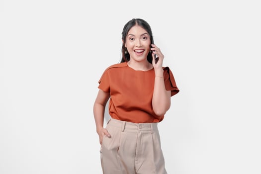 Cheerful young Asian woman wearing brown shirt smiling and having a call with someone, isolated by white background. photo