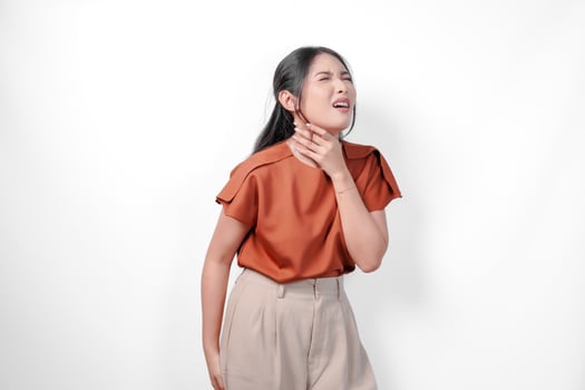 Young Asian woman in a brown shirt is holding her neck and chest, feeling unwell and coughing as symptom for cold, isolated by white background. photo