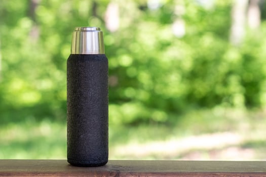 A black thermos with brewed tea or coffee stands on a wooden board with a copyspace. Thermos with hot drink photo