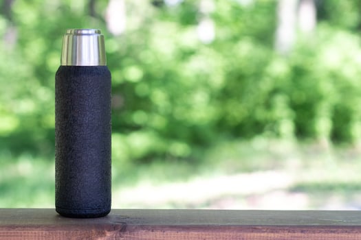 A black thermos with brewed tea or coffee stands on a wooden board with a copyspace. Thermos with hot drink photo