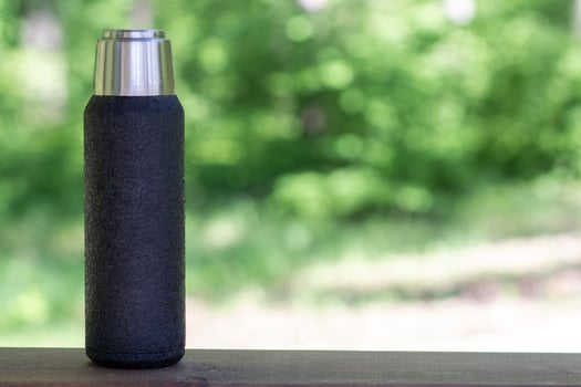 A black thermos with brewed tea or coffee stands on a wooden board with a copyspace. Thermos with hot drink photo