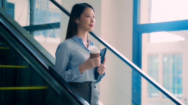 A business woman is walking down to escalator with a coffee cup in her hand photo