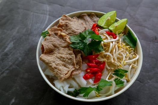 A Bowl Pho Bo traditional Soup with beef, rice noodles, ginger, lime, chili pepper in bowl. Close up. Vietnamese cuisine served on black background photo