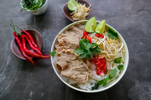 A Bowl Pho Bo traditional Soup with beef, rice noodles, ginger, lime, chili pepper in bowl. Close up. Vietnamese cuisine served on black background photo