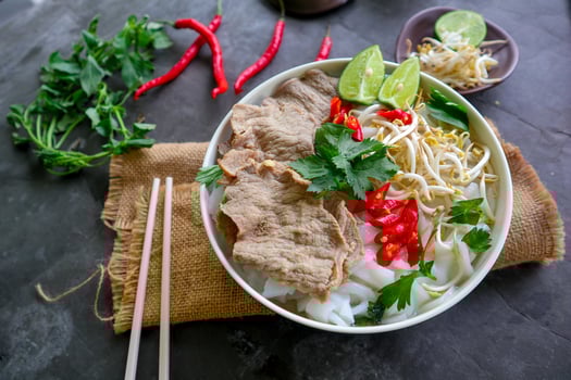 A Bowl Pho Bo traditional Soup with beef, rice noodles, ginger, lime, chili pepper in bowl. Close up. Vietnamese cuisine served on black background photo