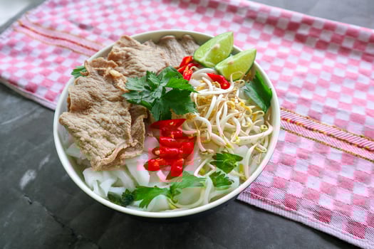 A Bowl Pho Bo traditional Soup with beef, rice noodles, ginger, lime, chili pepper in bowl. Close up. Vietnamese cuisine served on black background photo