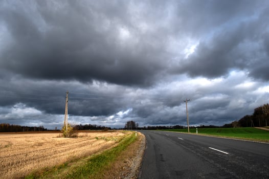 Dramatic sky with dark rain clouds over asphalt country road in autumn landscape photo