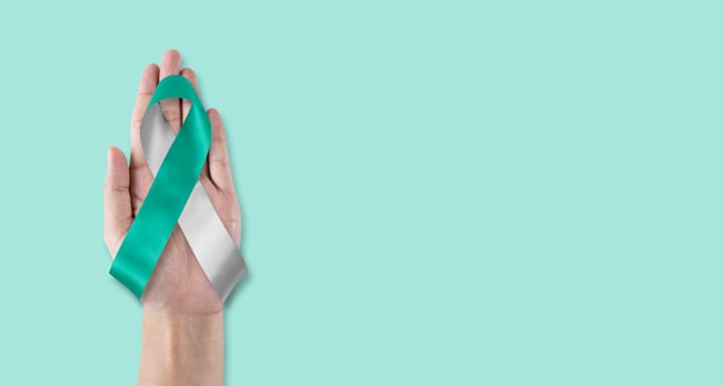Teal and white ribbon for cervical cancer awareness month in January and HPV prevention with bow on hand support photo