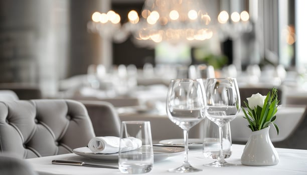 Elegant fine dining restaurant table setting with wine glasses, white tablecloth, and flower centerpiece under soft ambient lighting. photo
