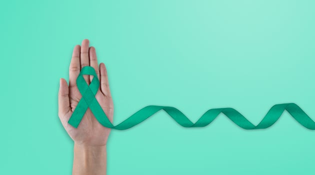 Hands holding emerald green or jade green ribbon on white fabric background with copy space, symbol for Liver Cancer awareness, World Cancer Day. Healthcare photo