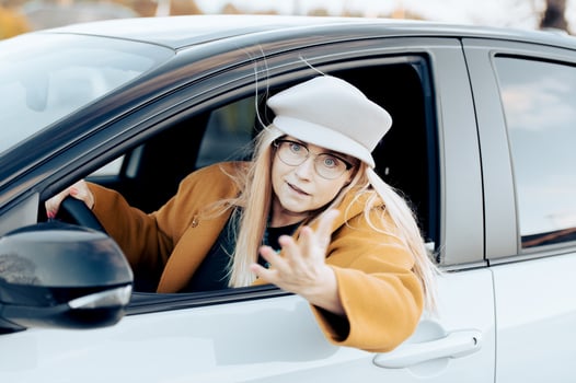excited middle aged flirtatious woman holding steering wheel gesturing and driving car photo