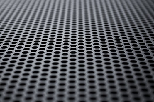 Perspective view on a the black metal surface with regular round holes. Industrial background photo